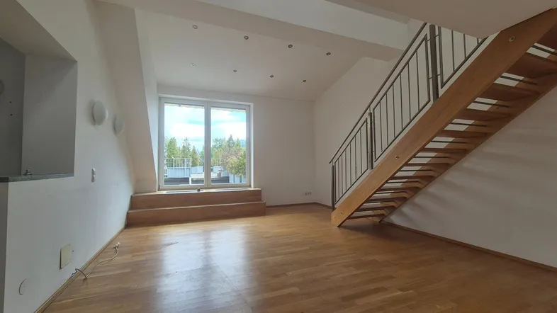 Helles Wohnzimmer mit Holzparkett, großen Fenstern und offener Holztreppe zum oberen Bereich.