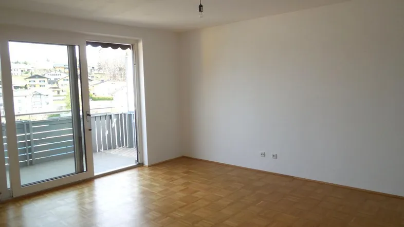 Helles Zimmer mit Parkettboden und Zugang zu einem Balkon, bietet einen weiten Blick auf die Umgebung.
