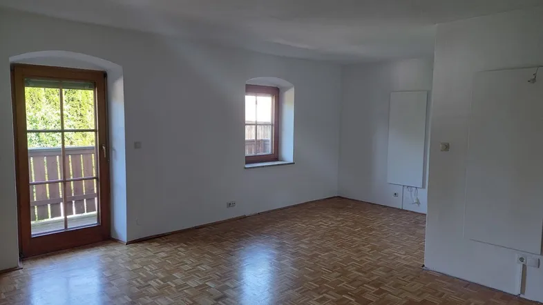 Heller Raum mit Parkettboden, weißen Wänden und Zugang zu einem Balkon.