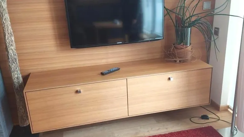 Modernes Wohnzimmer mit Wandfernseher, schwebendem TV-Möbel und rotem Teppich.