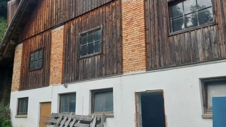Altes Bauernhaus mit verwitterter Holzfassade und Ziegelakzenten, das umfassende Renovierungsarbeiten benötigt.
