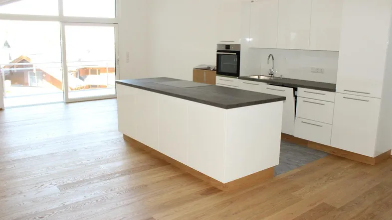 Moderne Küche mit weißer Hochglanzfront, Kücheninsel und Zugang zu einem sonnigen Balkon.