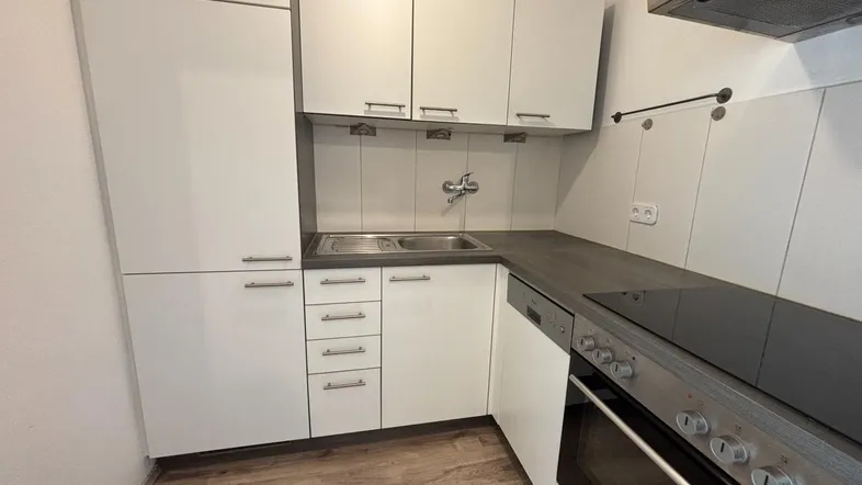 Moderne Einbauküche mit weißen Schränken, dunkler Arbeitsplatte und integrierten Geräten.