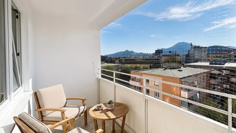Heller Balkon mit Holzsitzmöbeln und weitem Blick auf die Berge und die Stadt.