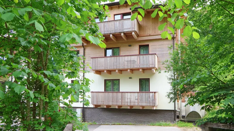 Mehrstöckiges Gebäude mit Holzfassade und mehreren Balkonen, umgeben von üppigem Grün.