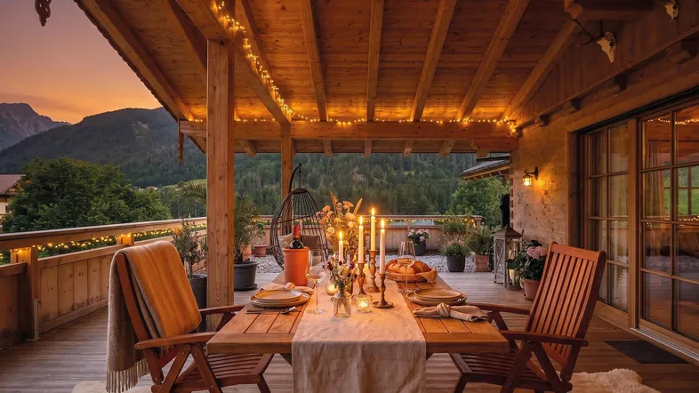 Gemütliche Holzterrasse mit Esstisch, Lichterketten und Bergblick bei Sonnenuntergang.