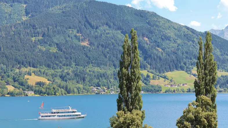 Panoramablick auf den See mit Bergen und einem Schiff unter blauem Himmel.