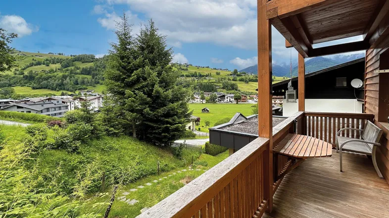 Geräumiger Balkon mit Holzboden und Geländer, bietet einen weiten Blick auf die grüne Landschaft und die umliegenden Berge.