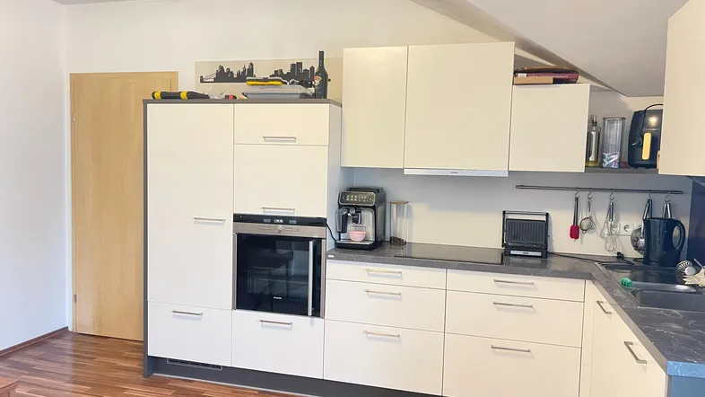 Moderne Einbauküche mit hellen Schränken, integriertem Backofen und Holzboden unter einer Dachschräge.