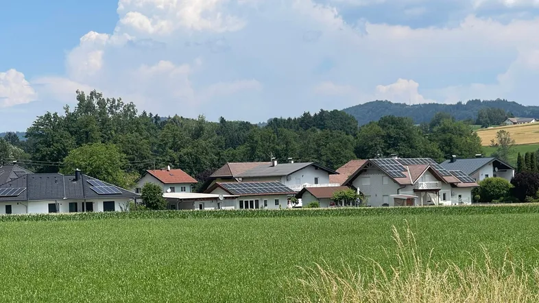 Ländliche Ansicht einer Siedlung mit Häusern, umgeben von Feldern und grünen Hügeln.