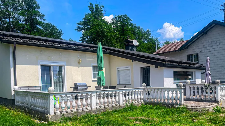 Helle Terrasse mit Grillbereich und Sitzgelegenheiten vor dem Haus unter blauem Himmel.