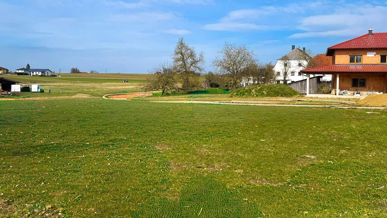Weitläufiges grünes Grundstück mit Blick auf umliegende Häuser und ländliche Umgebung unter blauem Himmel.