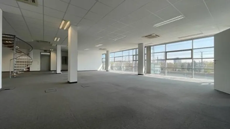Geräumiges, offenes Büro mit Teppichboden, großen Fenstern und einer Wendeltreppe, die zu einer weiteren Etage führt.