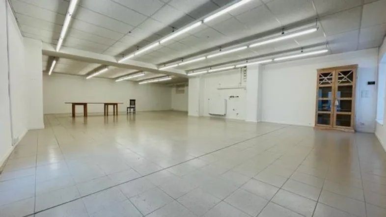 Großer, leerer Raum mit Fliesenboden und Deckenleuchten, ideal für gewerbliche Nutzung.