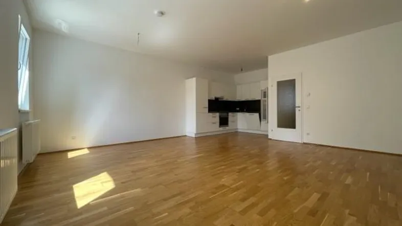Heller offener Wohnbereich mit Parkettboden und integrierter moderner Küche, ideal für geselliges Beisammensein.