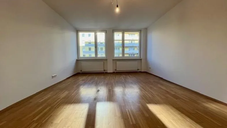 Helles, leeres Zimmer mit Parkettboden und zwei Fenstern, bereit zur individuellen Gestaltung.