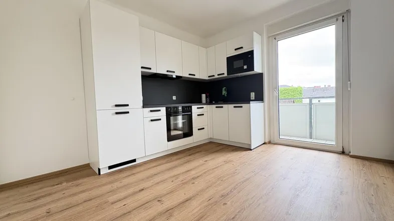 Moderne weiße Küche mit integrierten Geräten, Laminatboden und Zugang zum Balkon.
