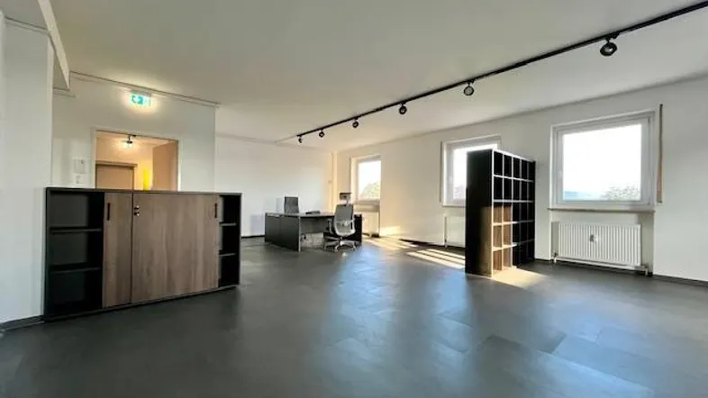 Großes, offenes Büro mit moderner Einrichtung, dunklem Boden und viel Tageslicht durch die Fenster.