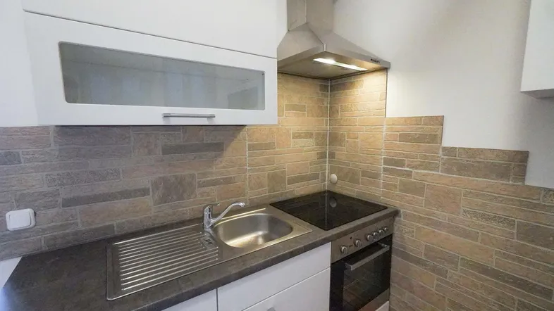 Kleine, funktionale Küche mit weißen Schränken, Spüle, Kochfeld und einer modernen Fliesenrückwand.
