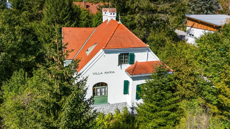 Luftaufnahme einer charmanten weißen Villa mit rotem Ziegeldach, umgeben von üppigem Grün und Bäumen.