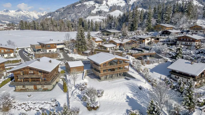 Winterliche Ansicht eines Chalet-Dorfes in den Bergen, umgeben von Schnee und Nadelbäumen.