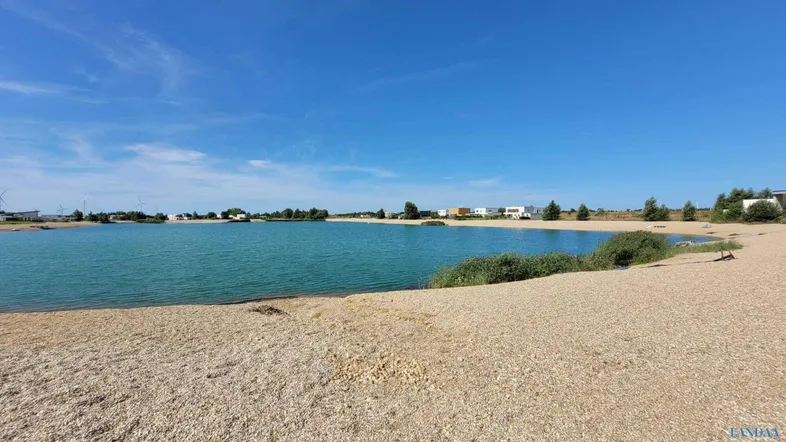 Weitläufiger Blick auf den See mit Sandstrand und die umliegende Naturlandschaft.