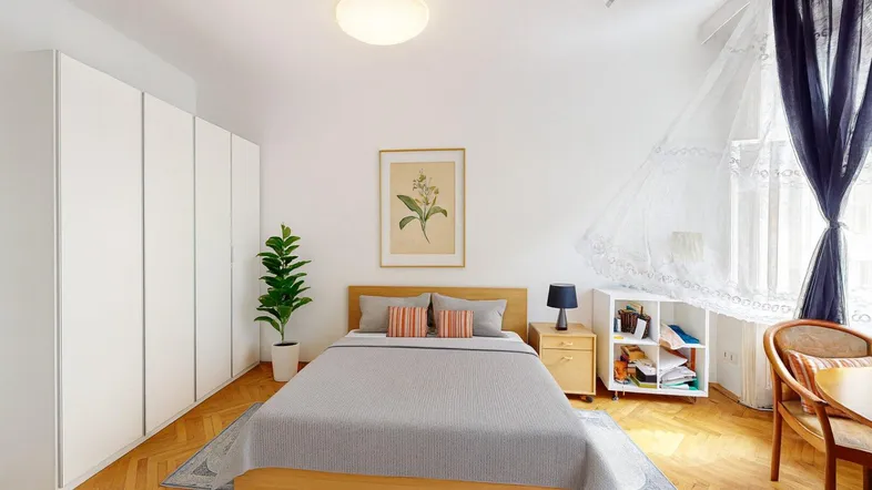 Helles Schlafzimmer mit Holzboden, großen weißen Kleiderschränken und einem Fenster mit Vorhängen.