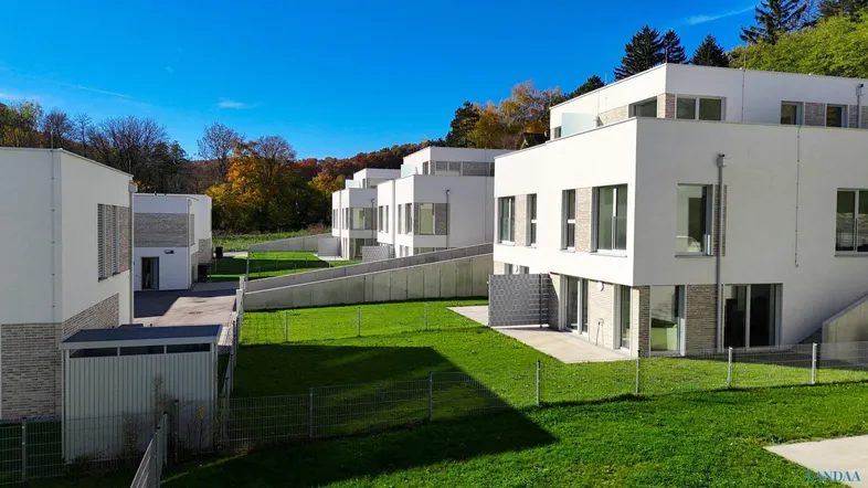 Moderne Reihenhäuser mit weißer Fassade und grünen Gärten in sonniger Umgebung.