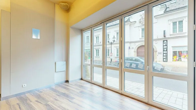 Heller Innenraum mit großen Fenstern zur Straße und Holzboden, ideal für ein Geschäft oder Büro.