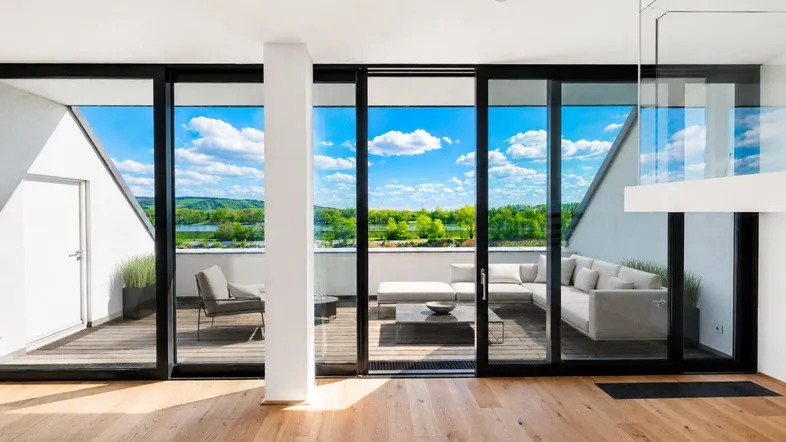 Heller Wohnbereich mit Holzboden und großen Glasfronten, die Zugang zu einer Terrasse mit Seeblick bieten.