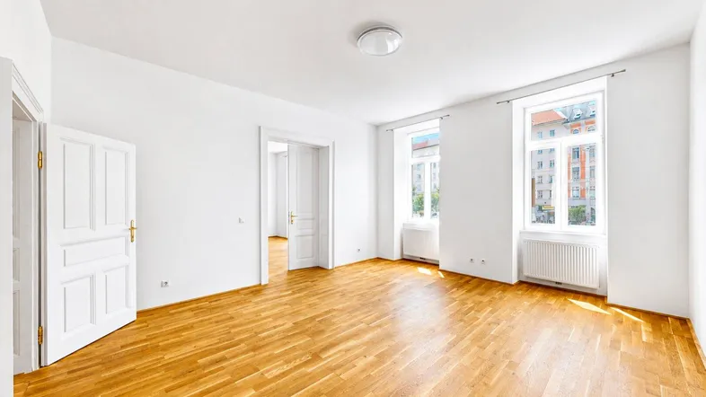 Helles, leeres Zimmer mit Parkettboden und hohen Fenstern, das als Wohnzimmer genutzt werden könnte.