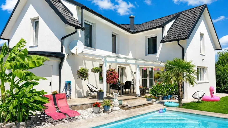 Modernes Haus mit Pool, großer Terrasse und Gartenmöbeln unter blauem Himmel.