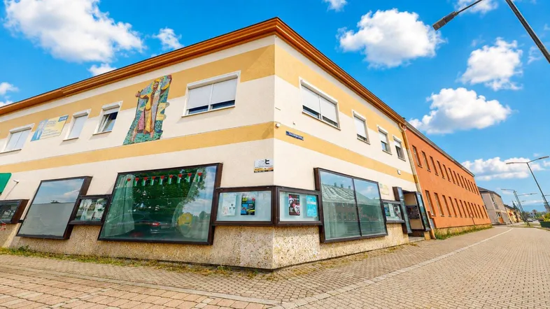 Gebäude mit gestreifter Fassade und großen Schaufenstern an einer Straßenecke unter blauem Himmel.