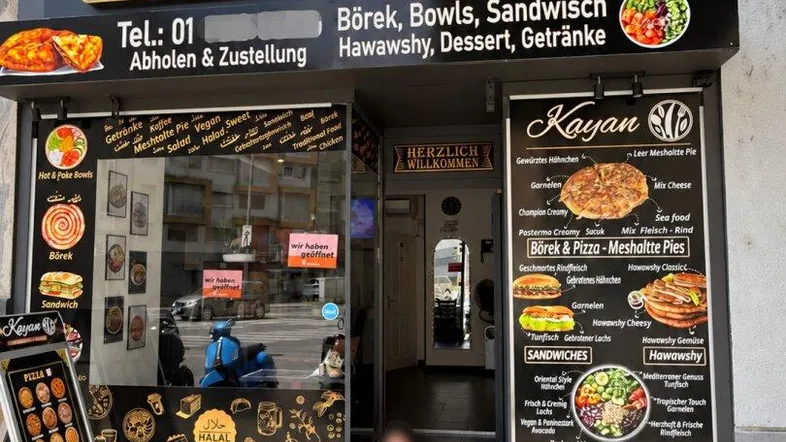 Die Außenansicht des Restaurants Kayan mit großer Beschilderung und Speisekarte am Eingangsbereich.