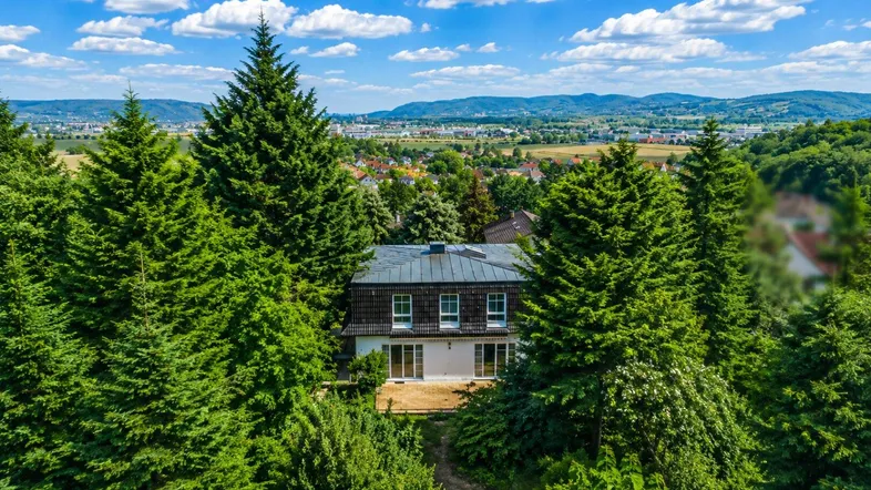 Luftaufnahme eines Hauses umgeben von Bäumen mit weitem Blick über die Landschaft und eine Stadt.