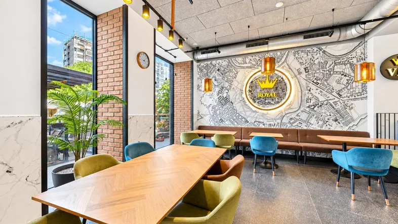 Geräumiger Restaurantbereich mit großen Fenstern, Ziegelwänden und modernen Möbeln in lebhaften Farben.