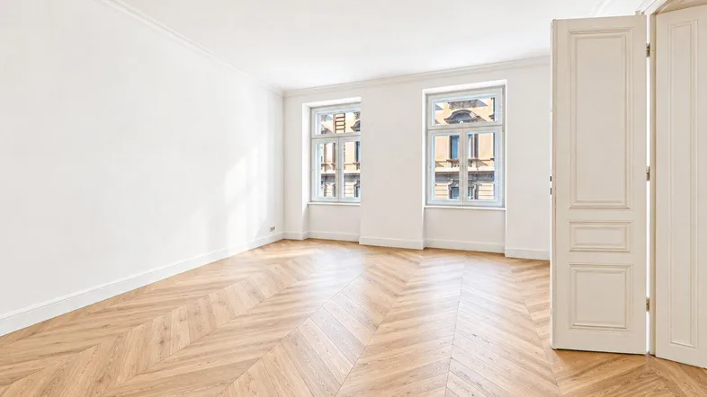 Helles Zimmer mit Fischgrätparkett, weißen Wänden und Blick auf die gegenüberliegende Fassade.