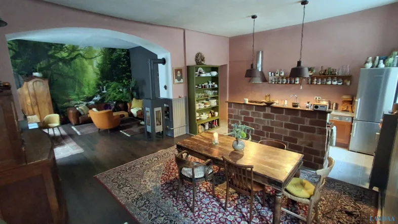 Offener Wohn- und Essbereich mit Holztisch, Kaminofen und einer dekorativen Waldtapete im Hintergrund.
