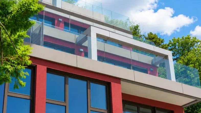 Modernes Gebäude mit roter Fassade, großen Fenstern und Glasbalkonen unter blauem Himmel.