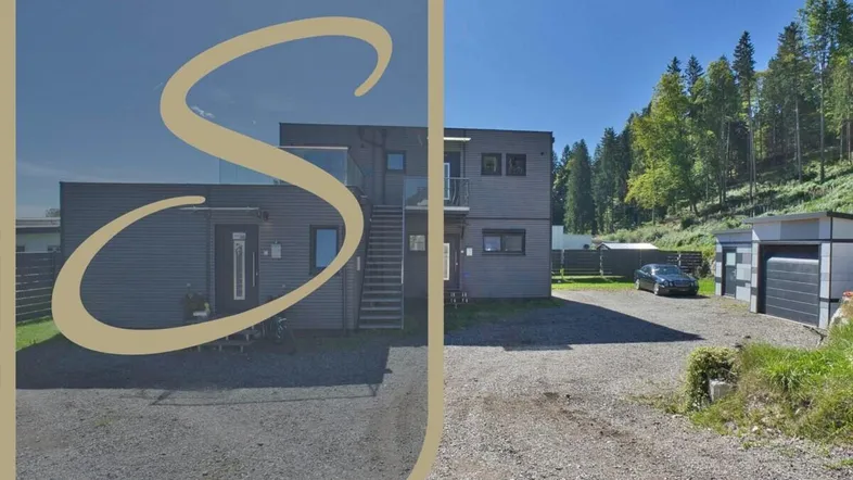Modernes Gebäude mit dunkler Holzfassade und Schotterzufahrt, umgeben von Bäumen.