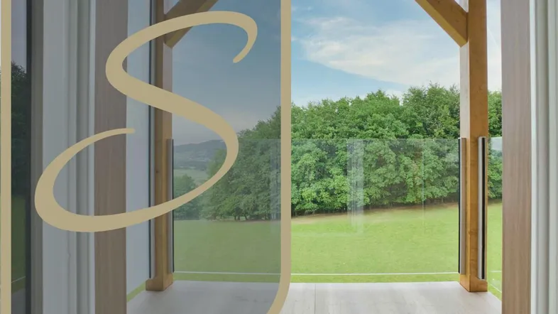 Balkon mit Holzkonstruktion und Glasgeländer, der einen weiten Blick ins Grüne bietet.