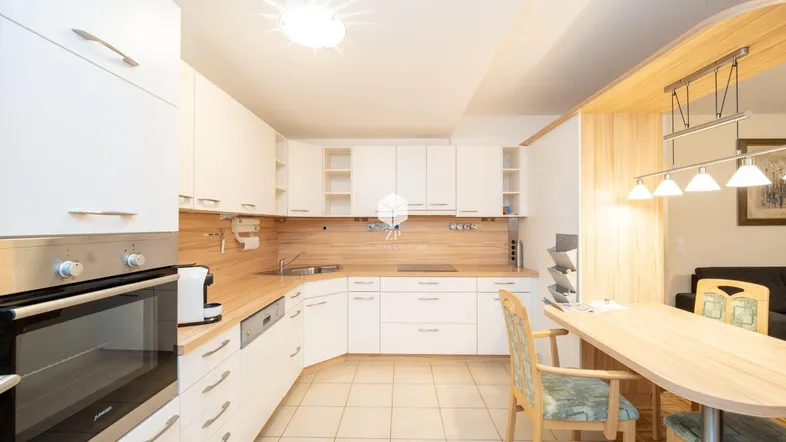 Moderne Küche mit weißen Schränken, Holzarbeitsplatte und integriertem Essbereich.