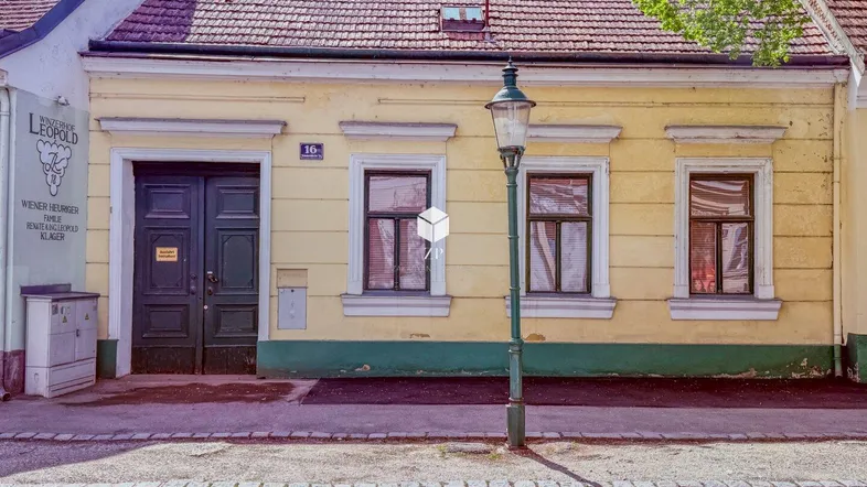 Gelbe Fassade eines älteren Gebäudes mit roten Dachziegeln und einer Laterne davor.