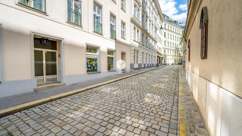 Historische Gebäude säumen eine gepflasterte Gasse unter blauem Himmel mit leichter Bewölkung.