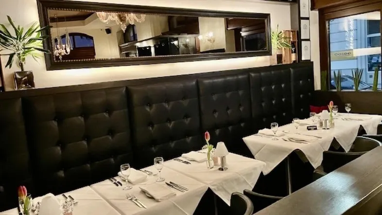 Gemütlicher Restaurantbereich mit gepolsterten Sitzbänken, elegant gedeckten Tischen und einem großen Spiegel.