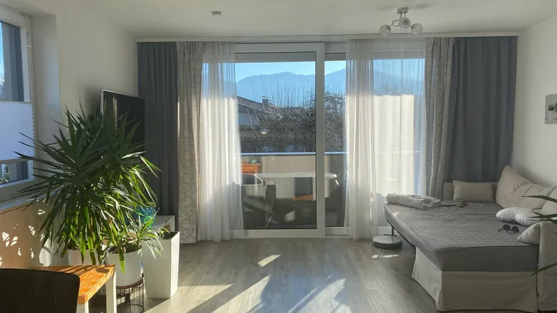 Helles Wohnzimmer mit Balkonzugang, großen Fenstern und Blick auf die Berge.