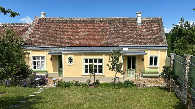 Charmantes Landhaus mit gelber Fassade, rotem Ziegeldach und gepflegtem Vorgarten unter blauem Himmel.