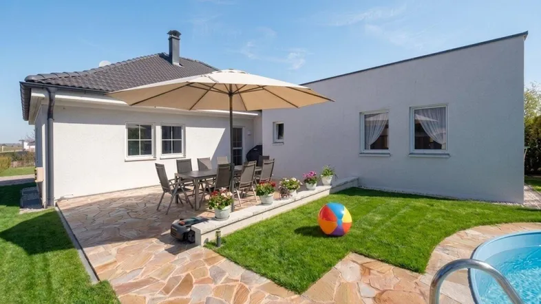 Sonnige Terrasse mit modernen Gartenmöbeln, gepflegtem Rasen und kleinem Pool am Haus.