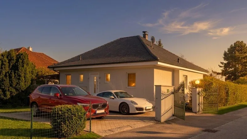 Einfamilienhaus mit gepflegter Auffahrt, zwei Autos und einem Eingangstor bei Sonnenuntergang.