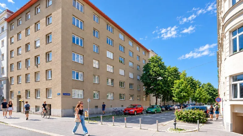 Mehrfamilienhaus in städtischer Umgebung mit gepflegter Fassade und Bäumen entlang der Straße.